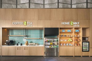 Una cafetería y tienda de té con una decoración moderna, que incluye una máquina de café, un área de estar y estantes llenos de diversos productos.