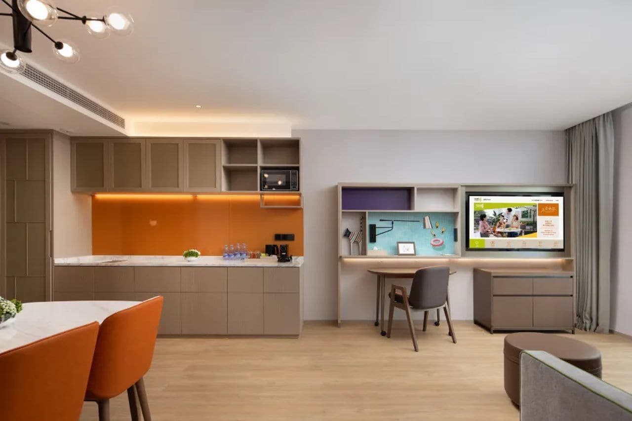 Una cocina moderna con electrodomésticos integrados, un comedor con sillas color naranja y un televisor de pantalla plana montado en la pared.