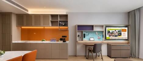 Una cocina moderna con electrodomésticos integrados, un comedor con sillas color naranja y un televisor de pantalla plana montado en la pared.