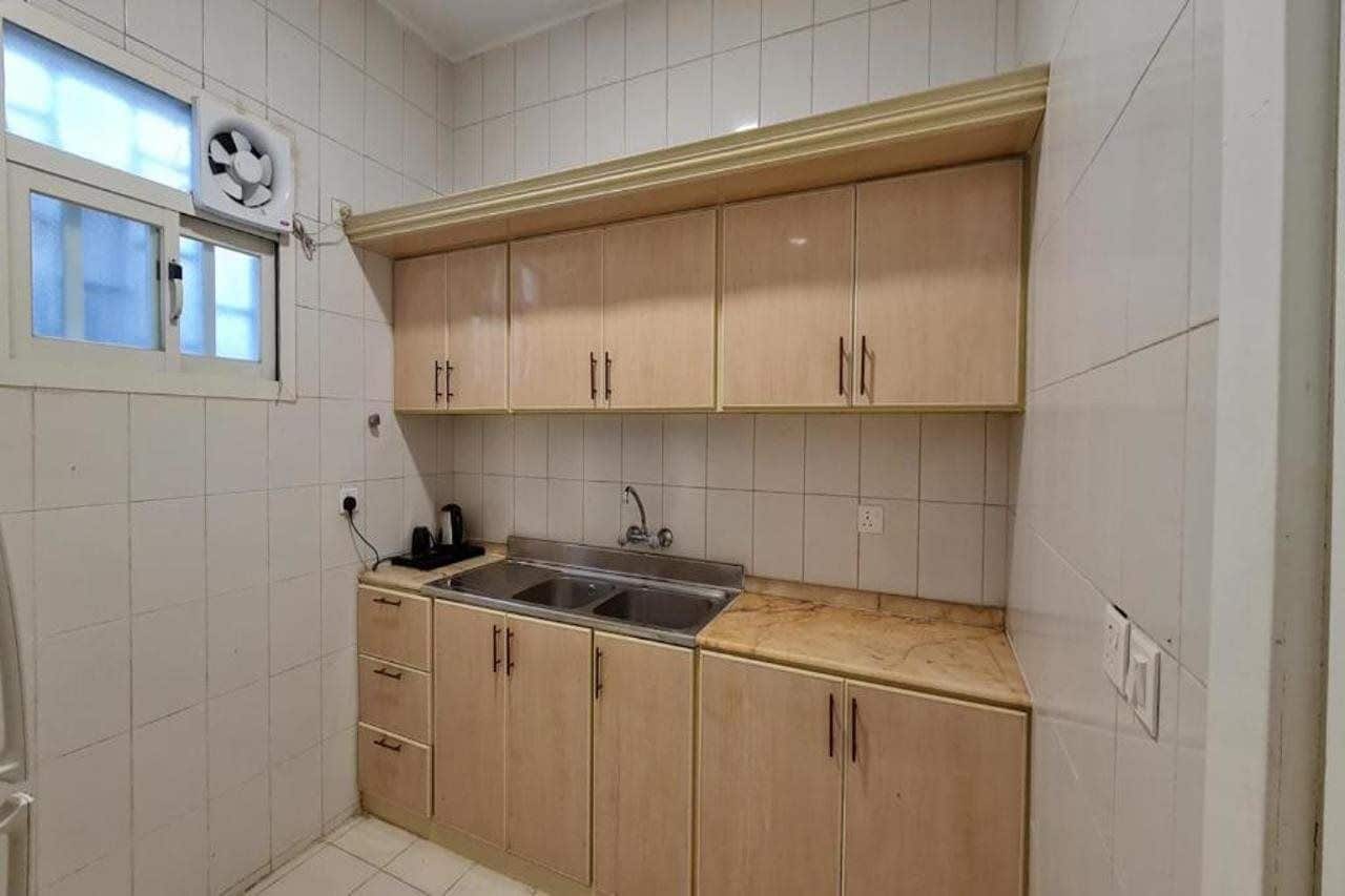 Une petite cuisine équipée d’un évier, de placards et d’une fenêtre avec un ventilateur.