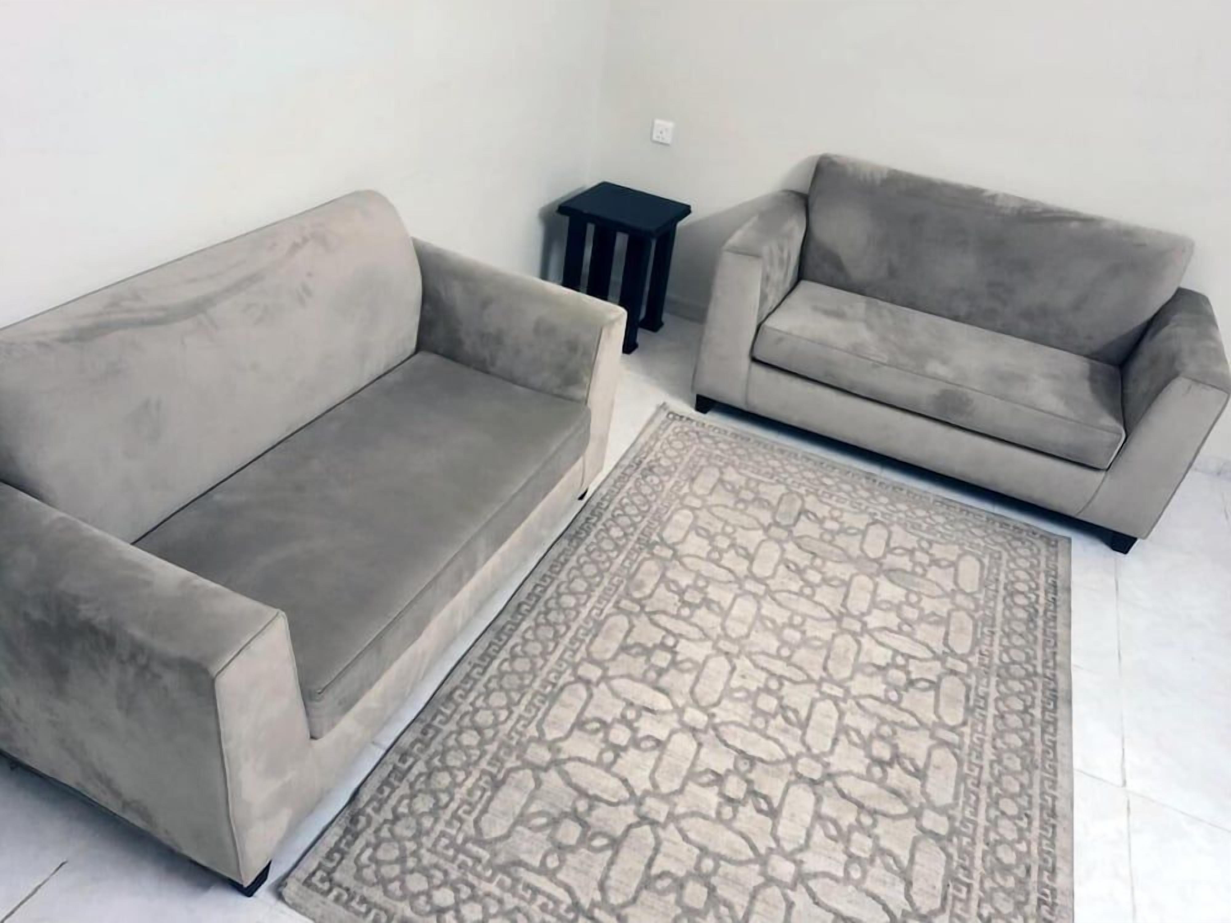 A living room with two grey sofas, a patterned rug, and a small black side table.