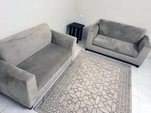 Una sala de estar con dos sofás grises, un tapete estampado y una mesita auxiliar negra.