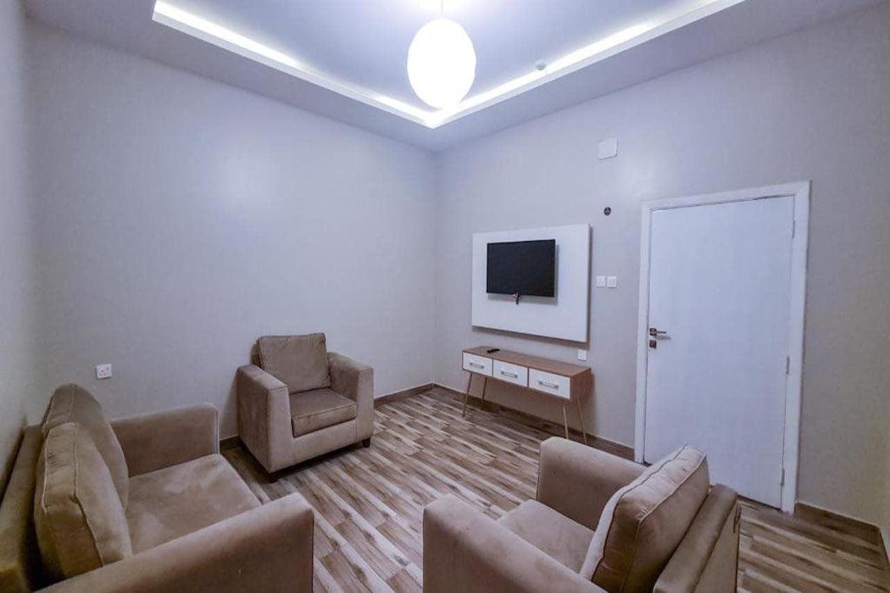 Una sala de estar con una televisión de pantalla plana montada en la pared, un sofá, una mesa de centro y una puerta.