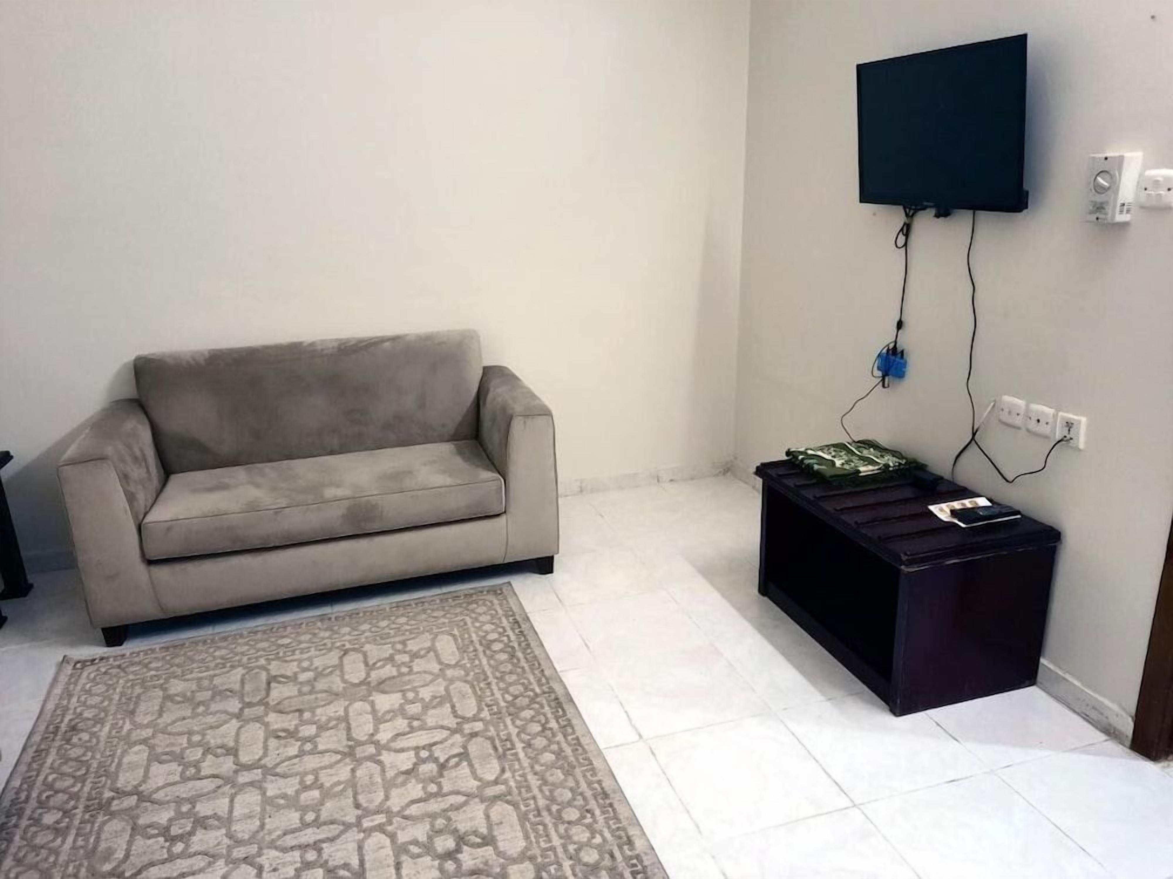 Un salon comprenant un canapé, un tapis à motifs, un meuble de rangement noir pour appareils électroniques et un téléviseur fixé au mur.