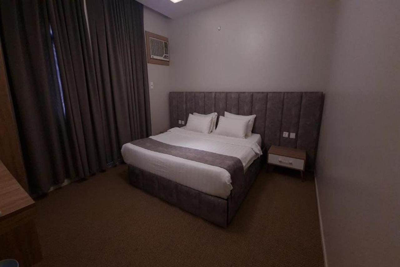 Habitació d'hotel amb un llit individual, una nitzeta, un calaix petit i una finestra amb cortines.