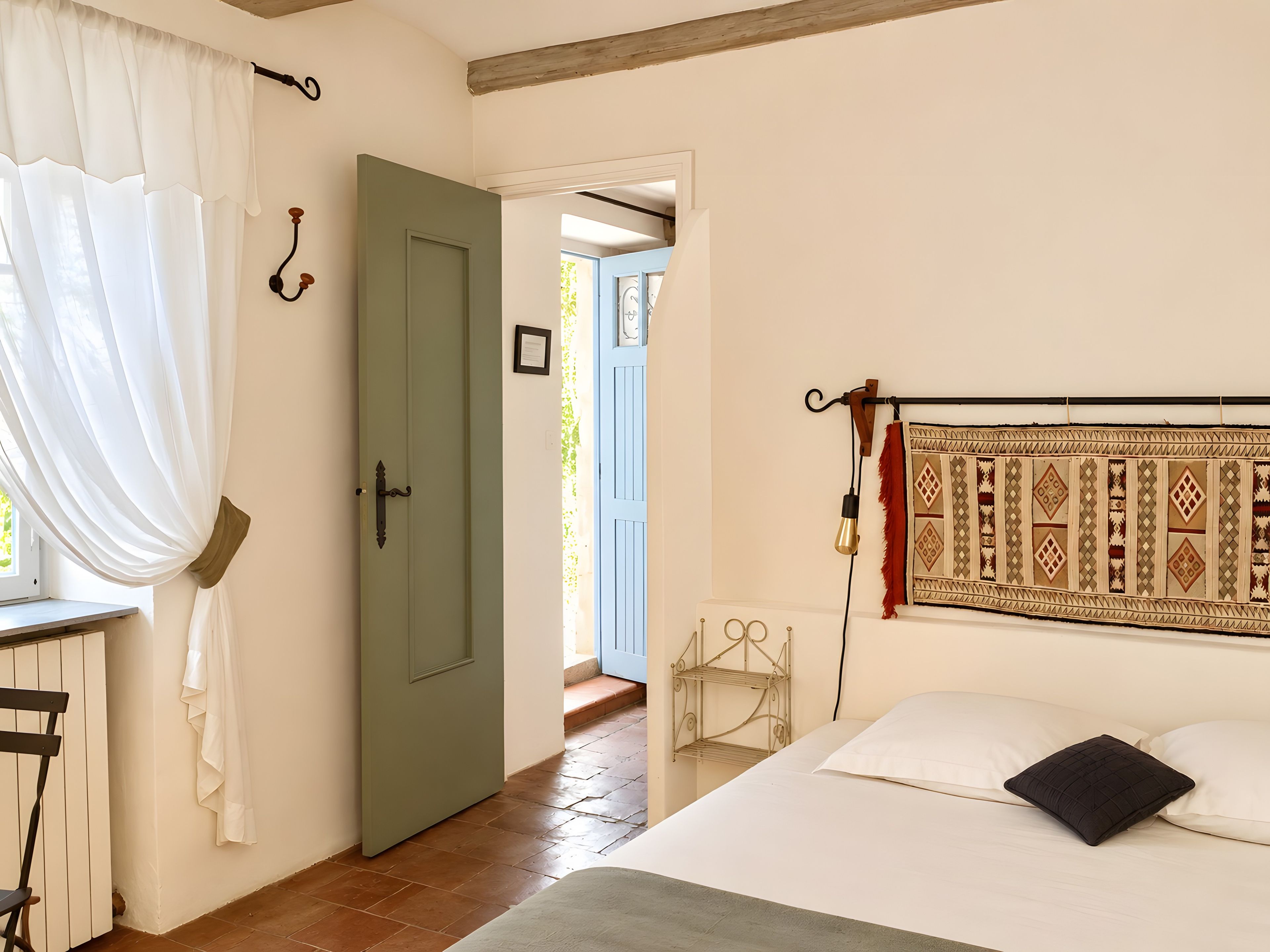 Een slaapkamer met een bed, een raam met gordijnen, een deur en een wandlamp.