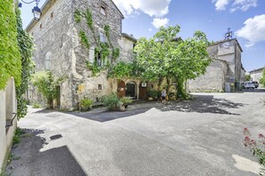 Un bâtiment en pierre avec une entrée centrale, une cour pavée et un véhicule garé au fond.