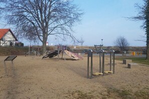 A playground with sand, metal structures, and a tree. - Holiday apartment with 2 bedrooms (Kölpinsee)
