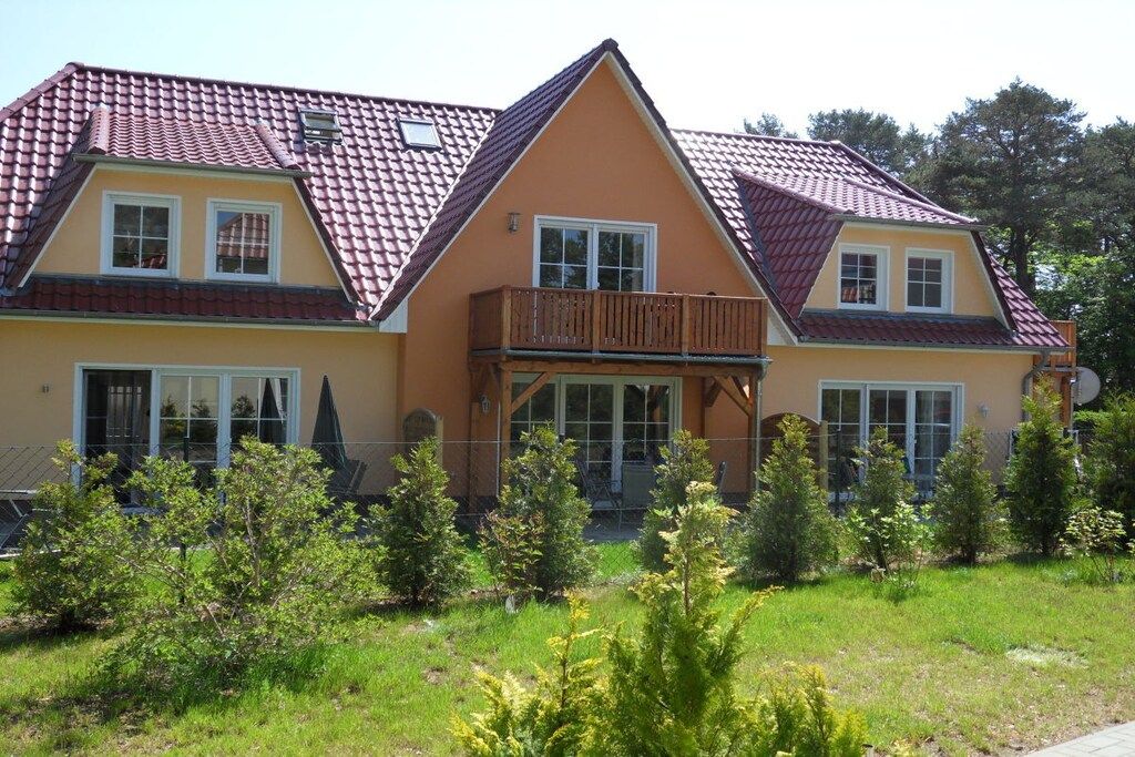 Uma casa de dois andares com varanda, telhado de telhas vermelhas e um jardim bem cuidado.