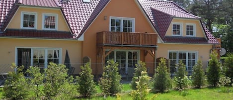 Uma casa de dois andares com varanda, telhado de telhas vermelhas e um jardim bem cuidado.