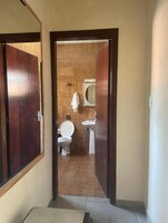 Un pasillo que conduce a un baño con inodoro, lavamanos y una toalla colgada en la pared.