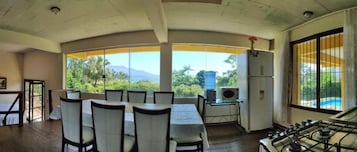 Una habitación con una mesa de comedor y sillas, un ventanal con vistas a zonas verdes y montañas, un refrigerador y una estufa a gas.