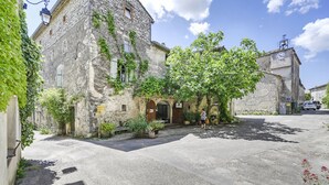 A stone building with a central entrance, a paved courtyard, and a vehicle parked in the background. - Charming Guest Room with Historic Character and Terrace (Fons-sur-Lussan)