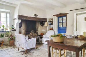 A rustic interior with a stone fireplace, white chairs, a wooden table with a basket, and a blue door. - Charming Guest Room with Historic Character and Terrace (Fons-sur-Lussan)