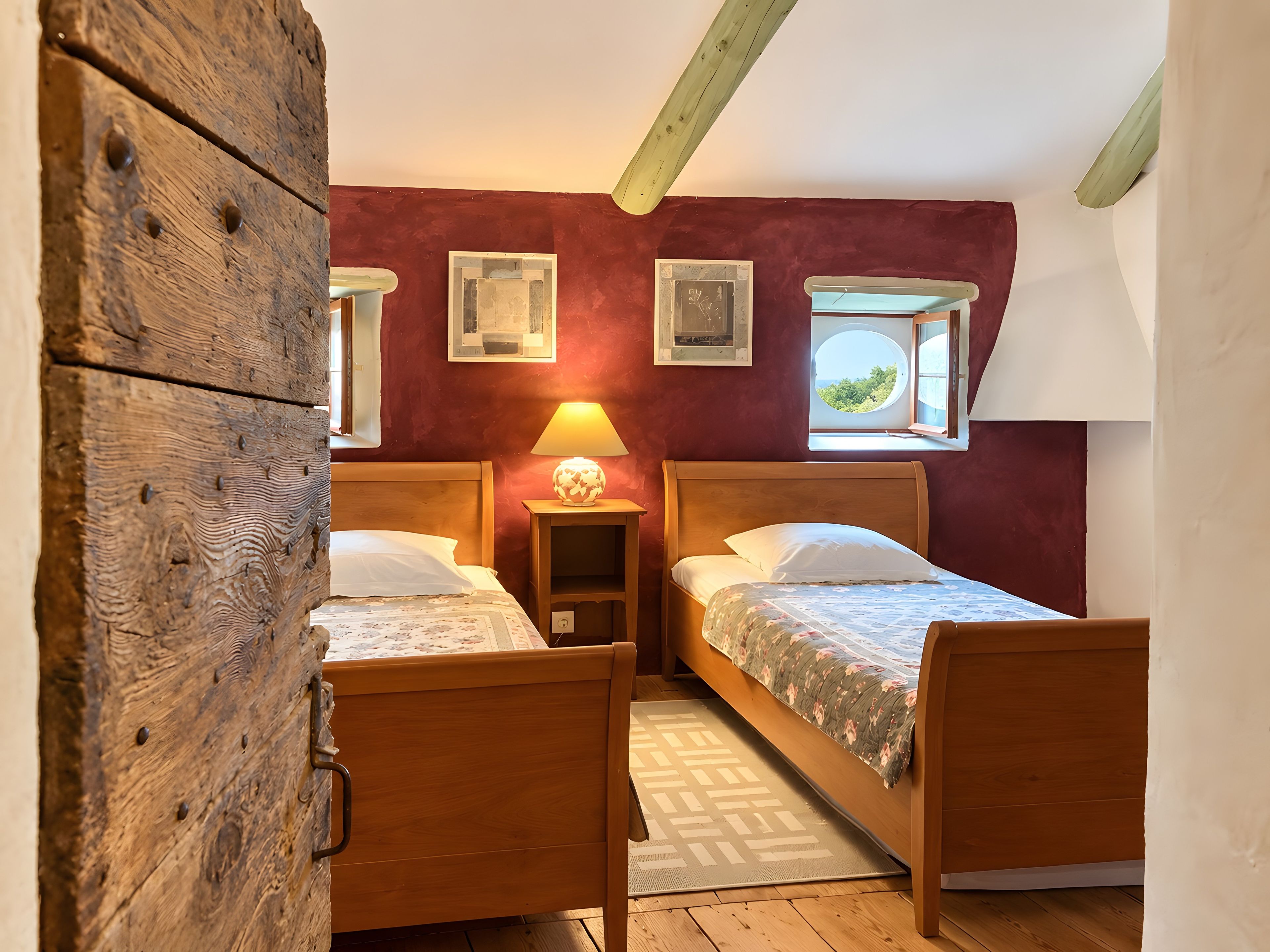 Une chambre avec deux lits en bois, une table de chevet avec une lampe et une fenêtre donnant sur un beau paysage.