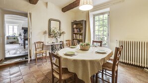 A dining area with a round table, chairs, a hanging light fixture, a bookshelf, and a window. - Charming Guest Room with Historic Character and Terrace (Fons-sur-Lussan)