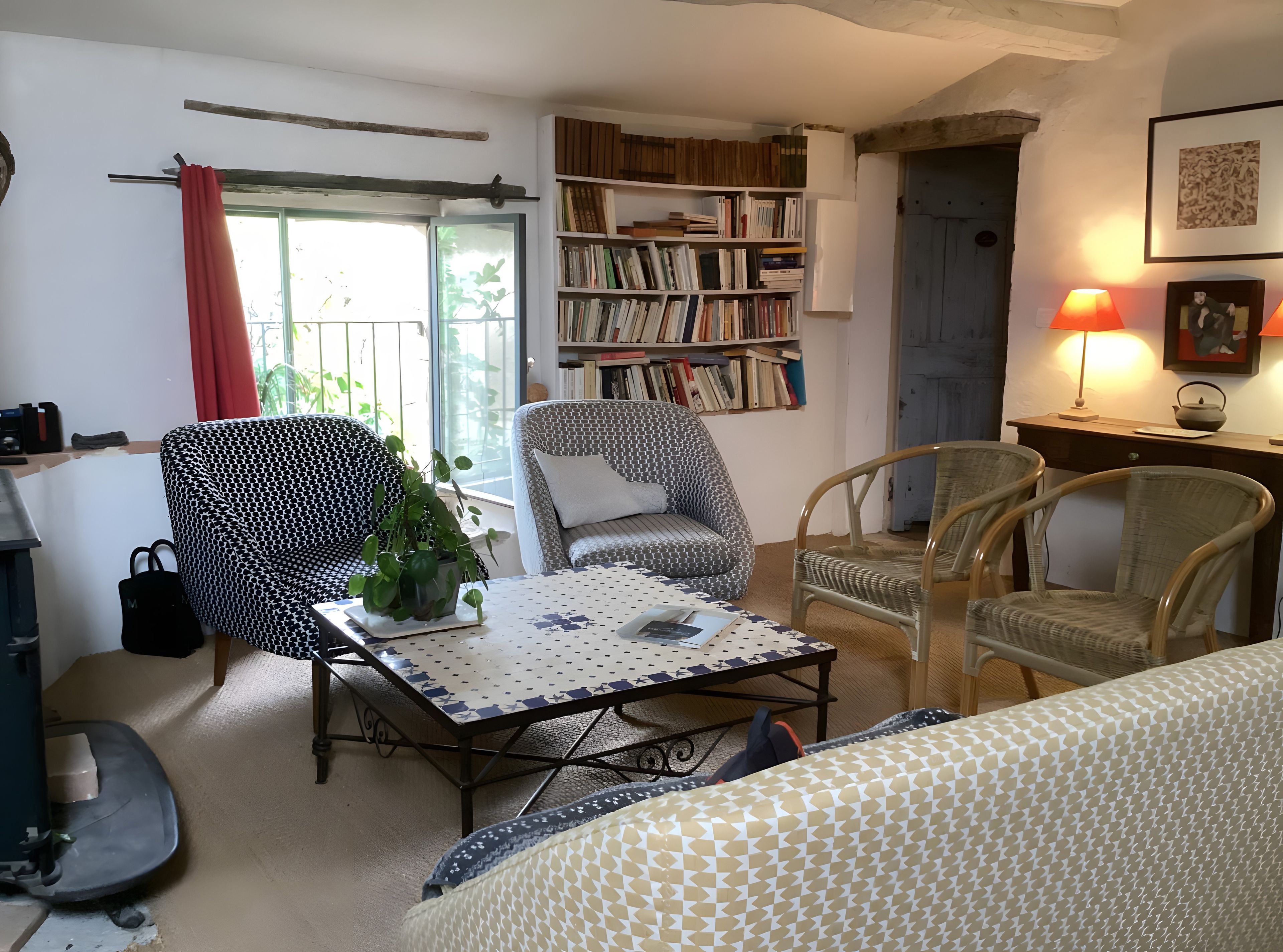 Een gezellige woonkamer met een boekenkast, twee gestreept beklede fauteuils, een bijzettafeltje met een plant in pot en een raam met gordijnen.