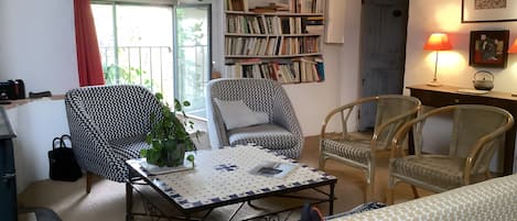 A cozy living room with a bookshelf, two patterned chairs, a small table with a potted plant, and a window with curtains.