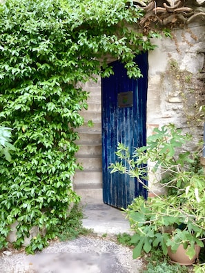 A blue door with a sign, surrounded by greenery and a stone wall. - Charming Guest Room with Historic Character and Terrace (Fons-sur-Lussan)