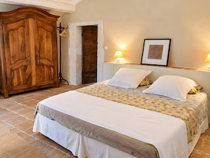 A bedroom with a large wooden wardrobe, a bed with floral bedding, and two bedside lamps. - Charming Guest Room with Historic Character and Terrace (Fons-sur-Lussan)