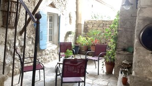 A stone-floored patio with outdoor seating, potted plants, and a rustic stone wall. - Charming Guest Room with Historic Character and Terrace (Fons-sur-Lussan)