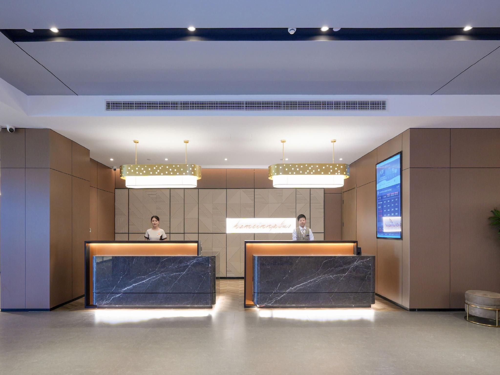 A hotel reception area with marble reception desks, a digital screen displaying information, and a modern ceiling design.