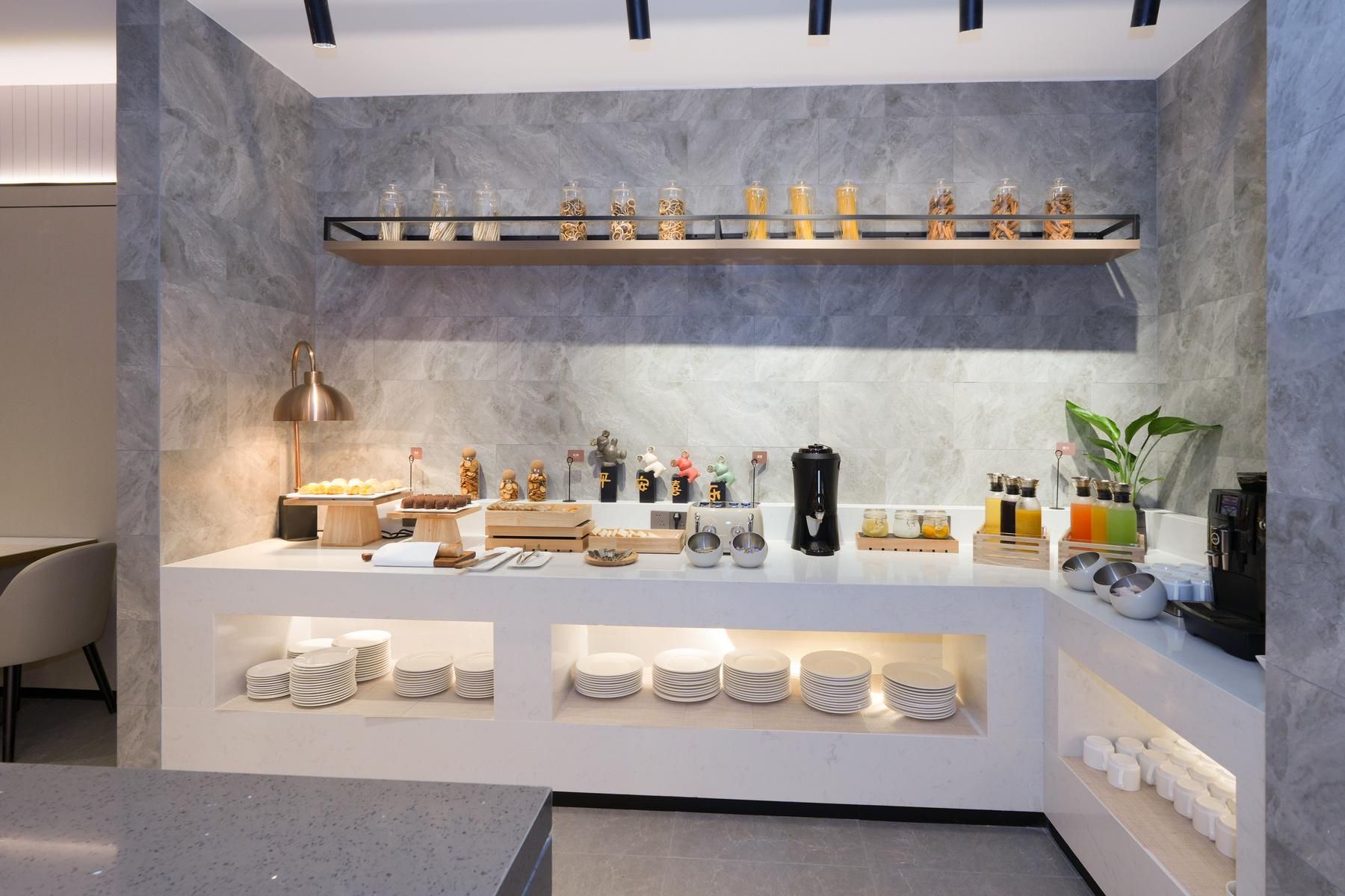 Een moderne keuken met marmeren wanden, een inbouwplank met potten, een koffieapparaat en netjes opgestapelde borden.
