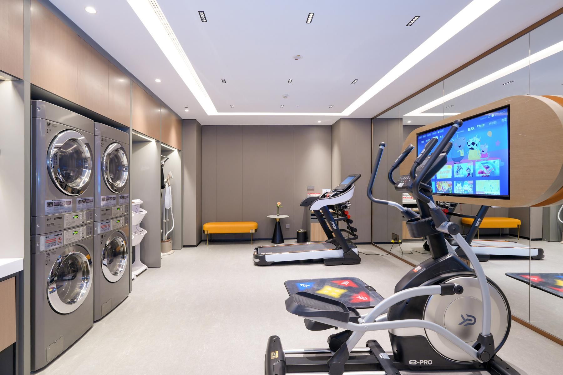 A modern laundry room with multiple washing machines, a bench, and a treadmill.