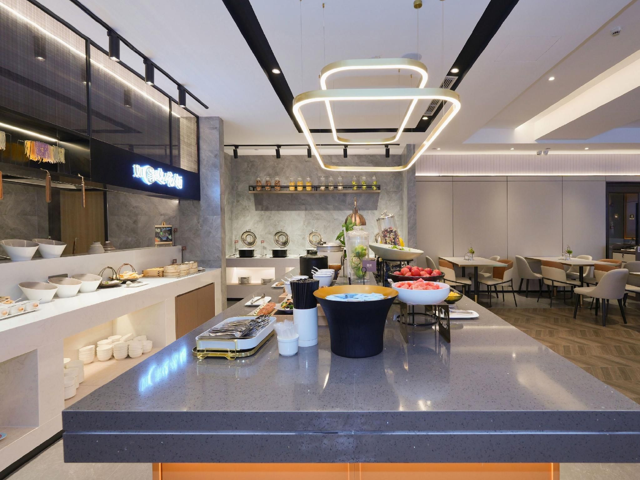 A modern hotel lobby with a central buffet area, seating arrangements, and a visible restaurant sign.