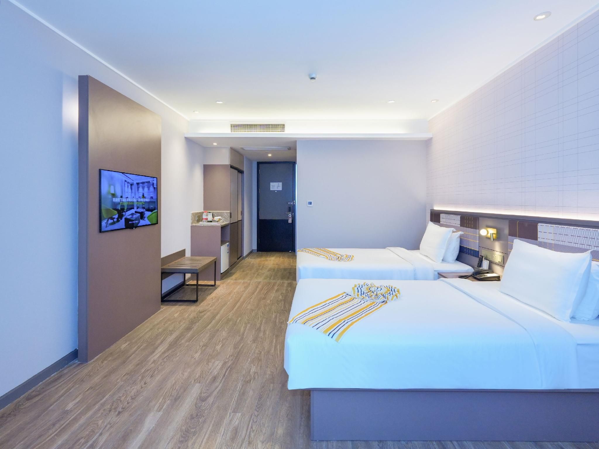 A hotel room with two beds, a television, a desk, and a small kitchenette.