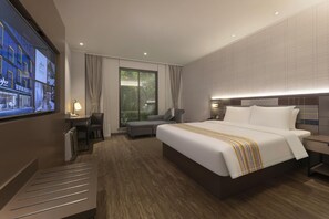 A modern hotel room with a large bed, a desk, a chair, a TV, and a view of greenery outside. - Homeinn Plus (Suzhou)