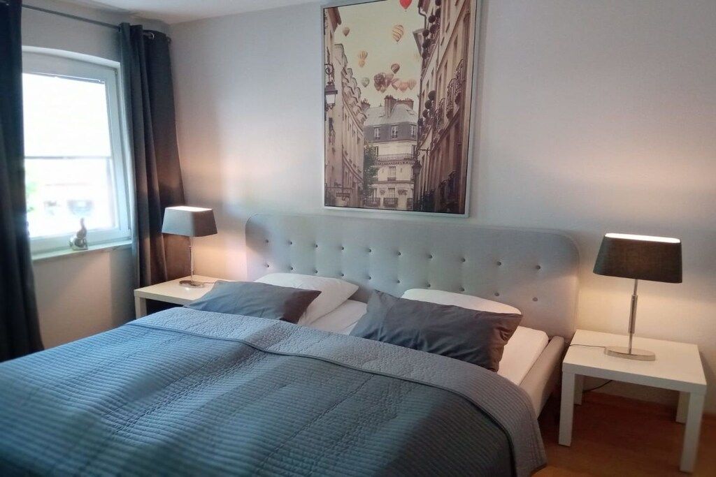 A bedroom with a bed, two bedside tables, a window with curtains, and a wall-mounted picture.
