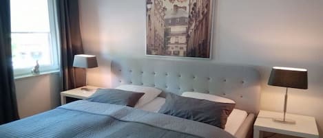 A bedroom with a bed, two bedside tables, a window with curtains, and a wall-mounted picture.