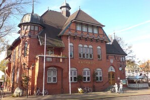 A red brick building with the name 'RATHAUS' on the facade, featuring multiple windows and a corner turret. - Holiday home with 1 bedroom (Stadt Fehmarn OT Burg)