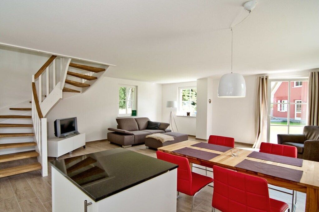 A modern living space with a dining area, a sofa, a TV, and a staircase.