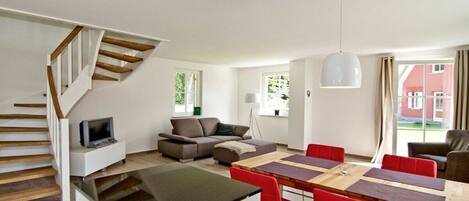 A modern living space with a dining area, a sofa, a TV, and a staircase.