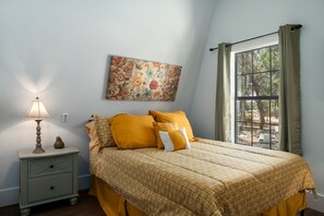 A bedroom with a bed, a nightstand, a lamp, a painting, and a window with curtains. - Terracotta Haven Hot Tub Pool Games Sleeps26 (Wimberley)