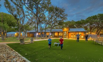 Una zona residencial con una casa y una estructura cubierta, rodeada de árboles y un césped cuidado.