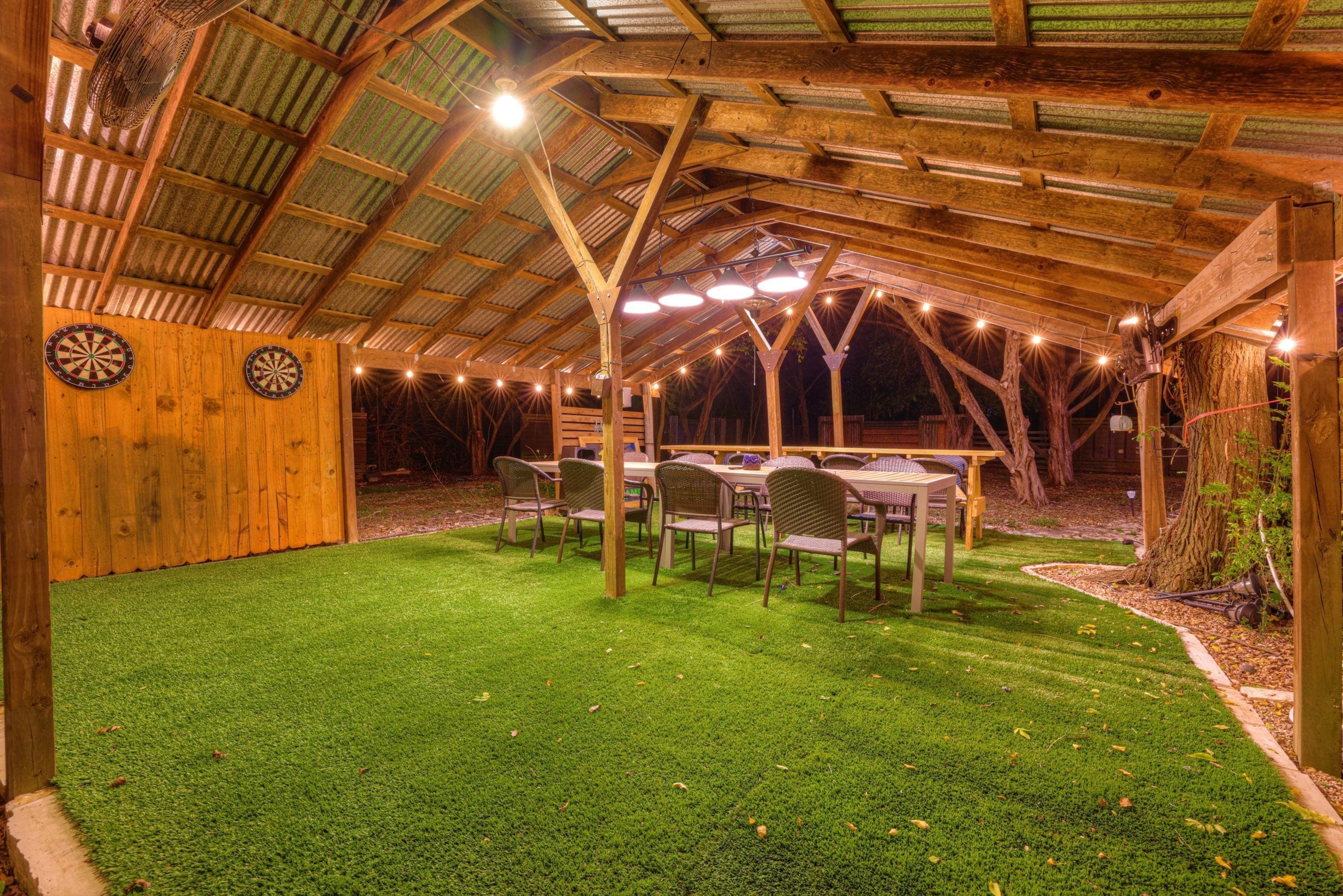 Un espacio al aire libre techado con una mesa, sillas, un dardo y luces artificiales.