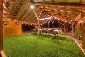 A covered outdoor area with a table and chairs, a dartboard, and artificial lighting. - Terracotta Haven Hot Tub Pool Games Sleeps26 (Wimberley)