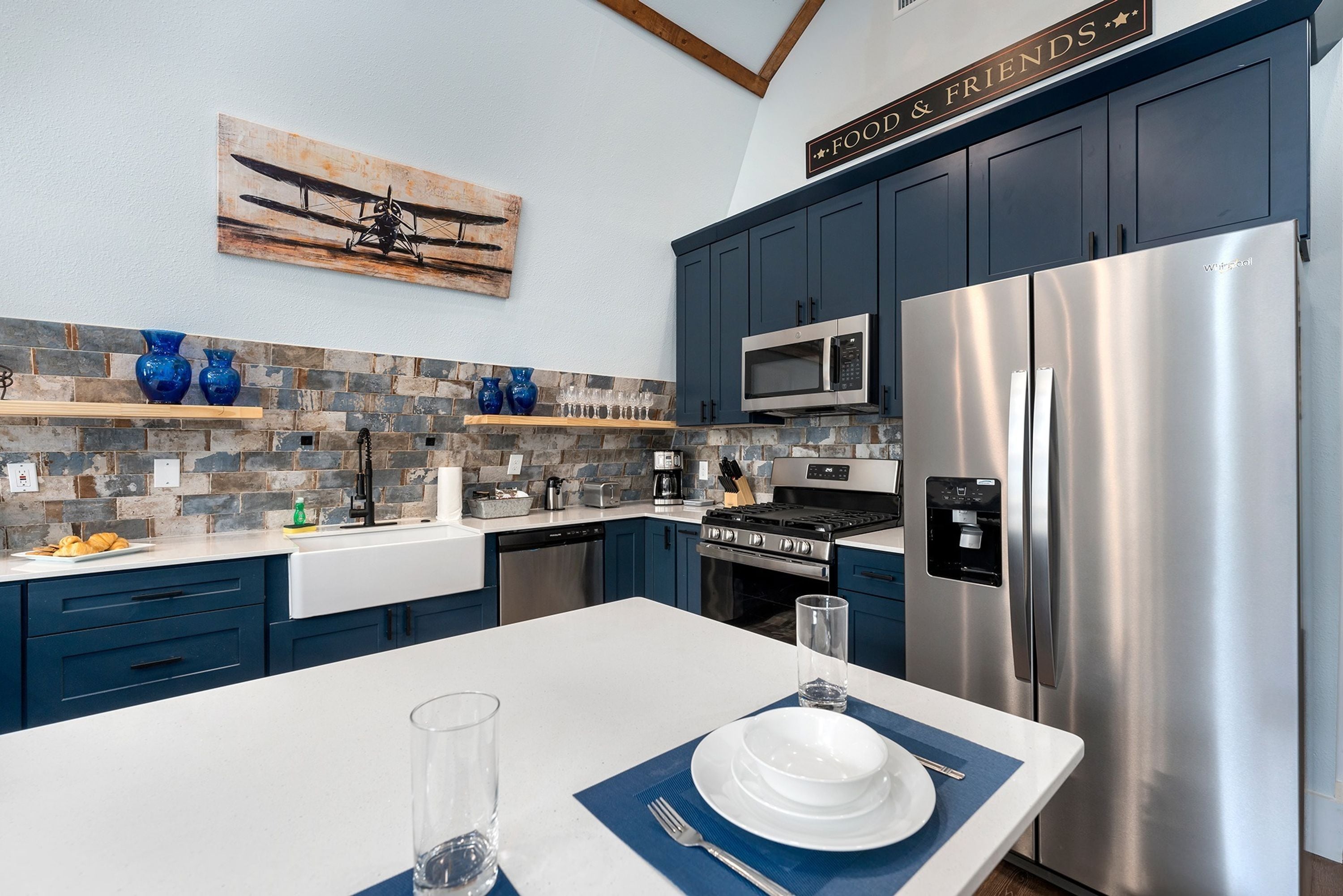 A modern kitchen with blue cabinets, stainless steel appliances, and a stone backsplash.