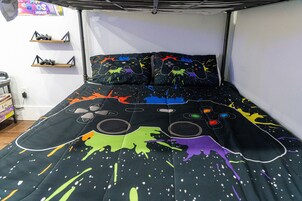 Una cama con un diseño de salpicadura de pintura negra y colorida, un estante con zapatos y una pared con un póster.