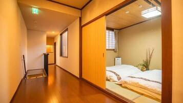 A hotel corridor with a wooden floor, a bed with white bedding, and a sliding door.