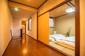 Corredor de hotel com piso de madeira, cama com roupa de cama branca e uma porta deslizante.