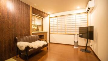 A room with a leather sofa, a flat-screen TV, a heater, and a window with blinds.