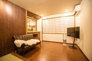 Quarto com sofá de couro, televisão de tela plana, aquecedor e janela com persianas.