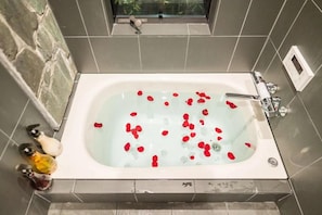 Una bañera con pétalos de rosa flotando en el agua, rodeada de azulejos grises y una pared de piedra.
