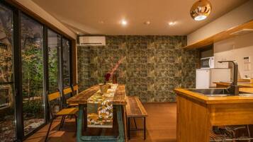 A modern kitchen with a wooden island, a dining table with chairs, and a view through large windows.