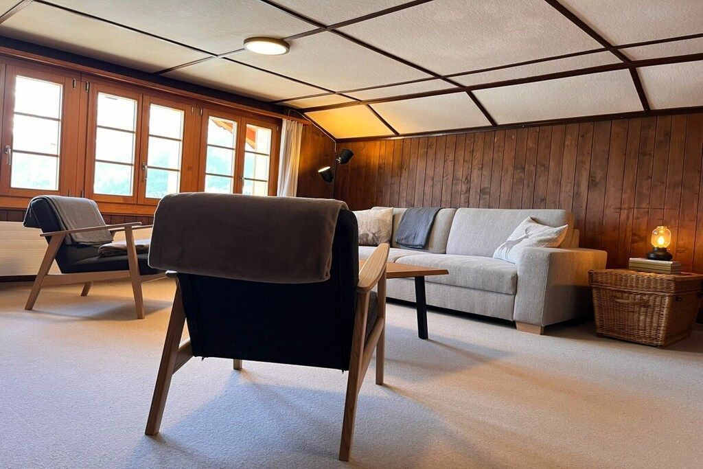 Ein gemütliches Zimmer mit einer Couch, einem Sessel, einer Lampe und einem Fenster mit Vorhängen.
