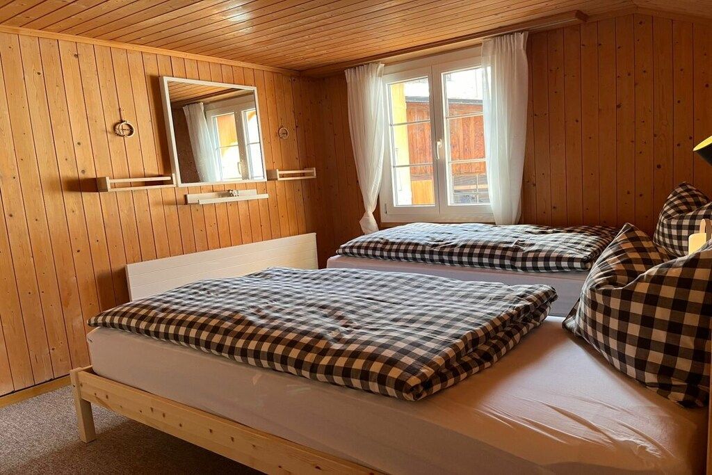 Ein Zimmer mit Holzwandverkleidung, zwei Betten mit karierten Bettbezügen, einem Spiegel und einem Vorhangfenster.